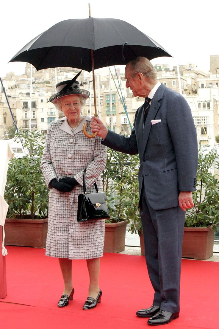 an older man and woman standing on a red carpet holding an umbrella over their heads