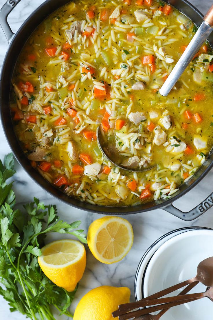 a pot filled with chicken noodle soup next to lemons and parsley