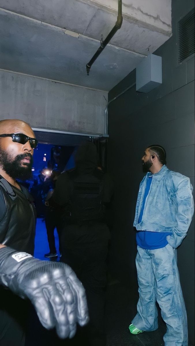 two men dressed in black and blue standing next to each other with one man wearing sunglasses