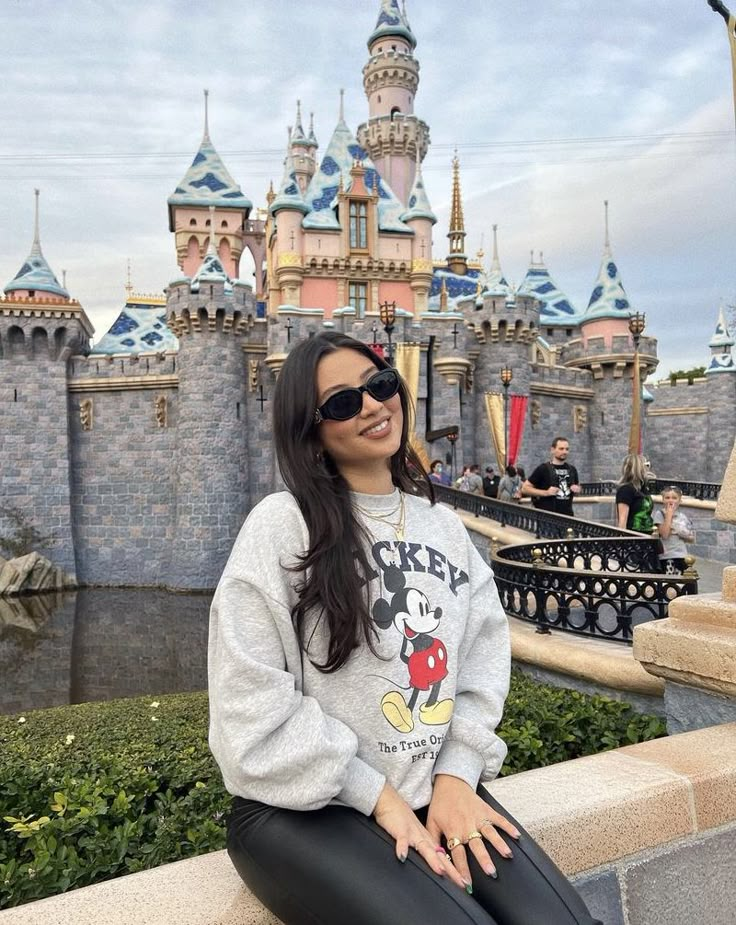 a woman sitting on the edge of a wall in front of a castle at disneyland