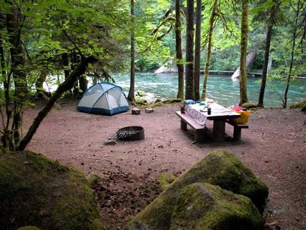 there is a picnic table with a tent in the woods next to some rocks and water