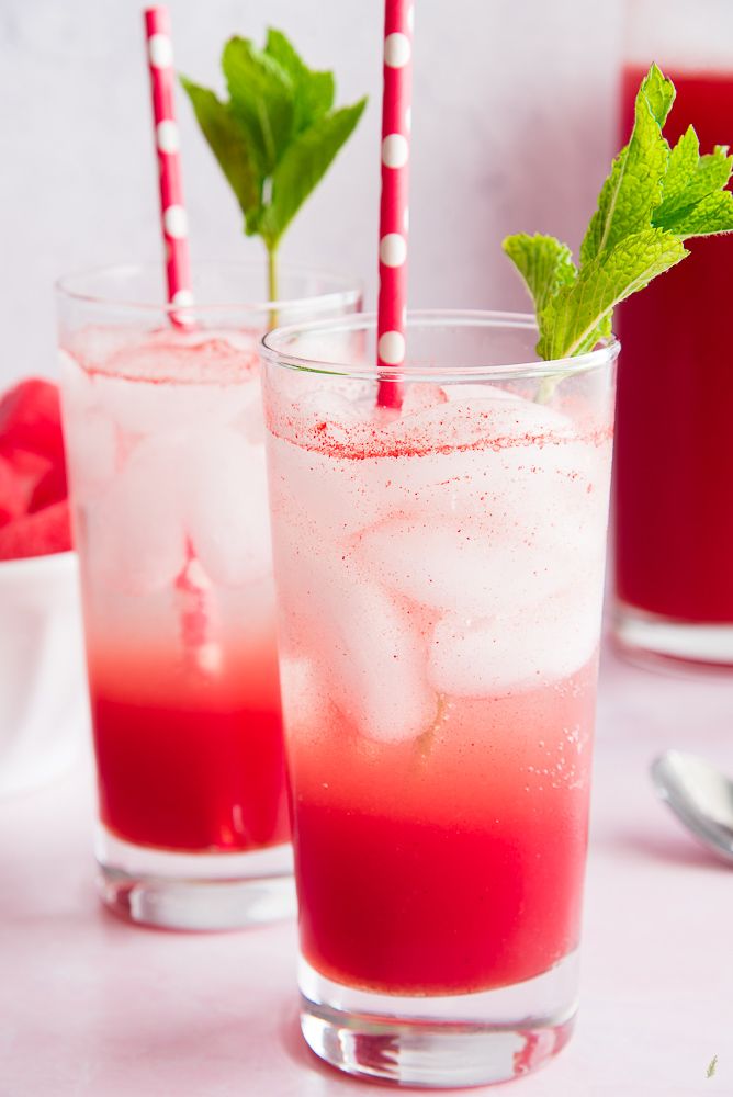 two glasses filled with red liquid and green leaves