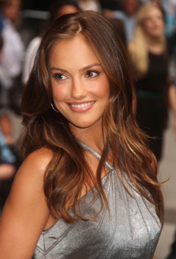 a beautiful young woman in a silver dress posing for the camera with people behind her