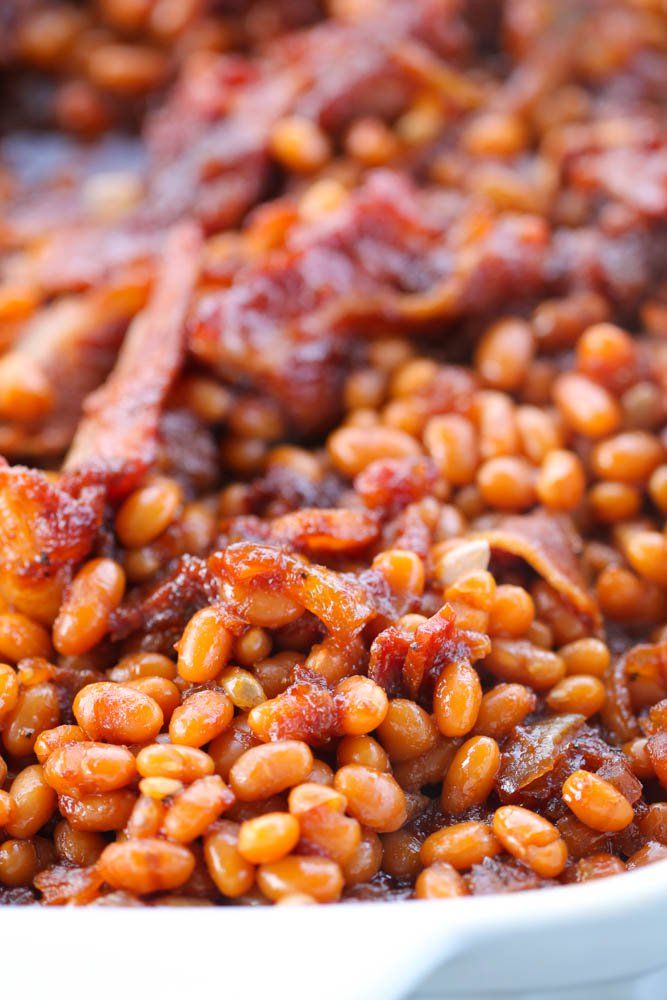 baked beans are being cooked in a white dish with bacon on top and other ingredients