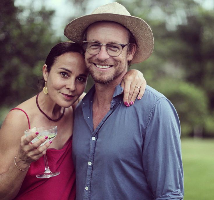 a man and woman standing next to each other holding wine glasses in front of trees