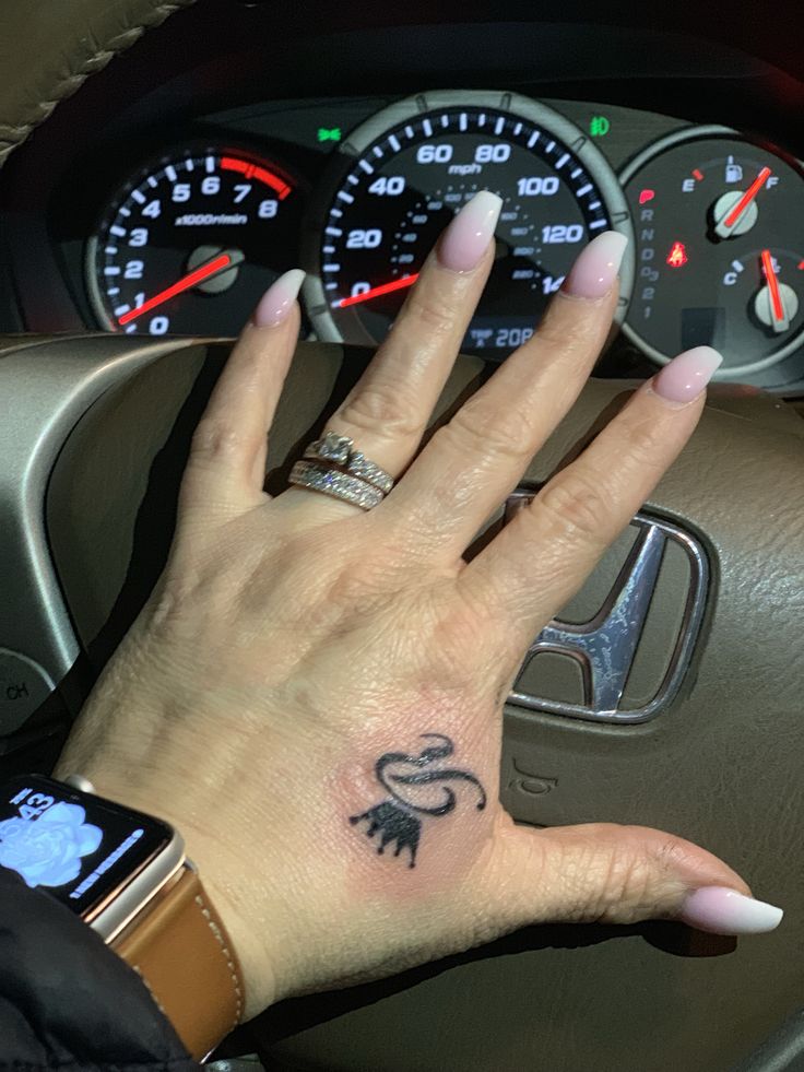 a woman's hand on the steering wheel of a car with an animal tattoo