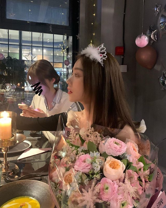 a woman sitting at a table with flowers and candles in front of her, wearing a tiara