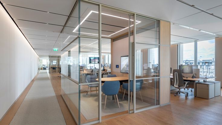 an office with glass walls and wooden flooring is pictured in this image, there are two desks on either side of the wall