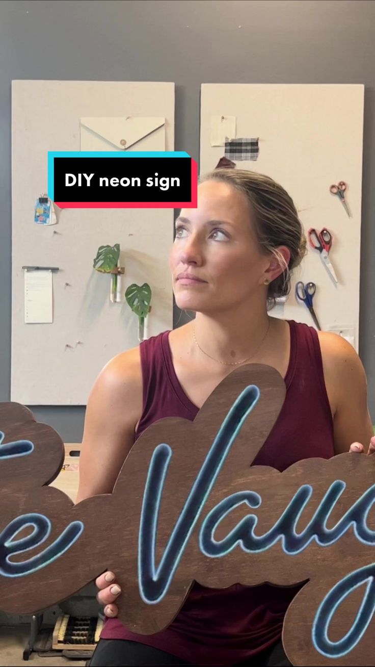 a woman holding up a wooden sign that says be unique in front of her face