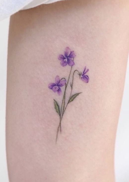 a small purple flower tattoo on the thigh