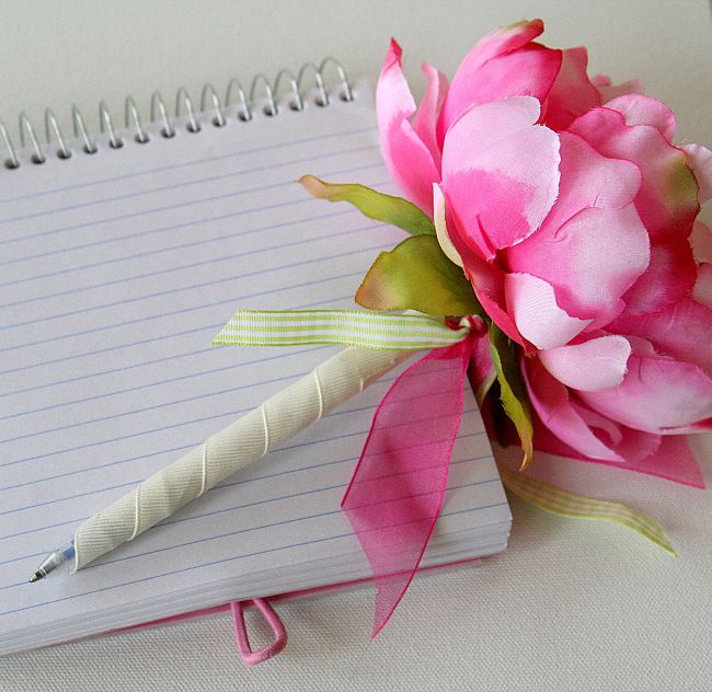 a pink flower sitting on top of a notepad next to a pen