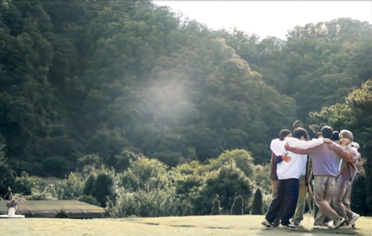 a group of people standing next to each other on a lush green field with trees in the background