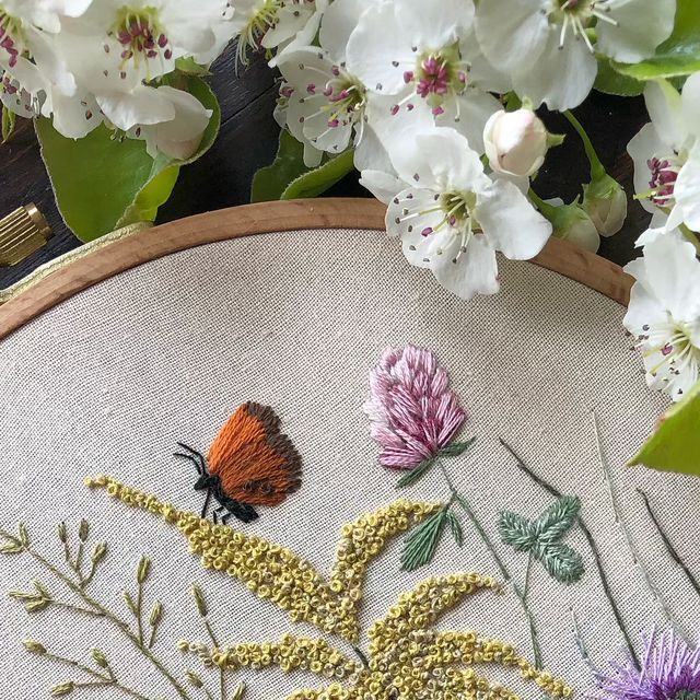 a close up of a embroidery on a wooden hoop with flowers in the background and a butterfly