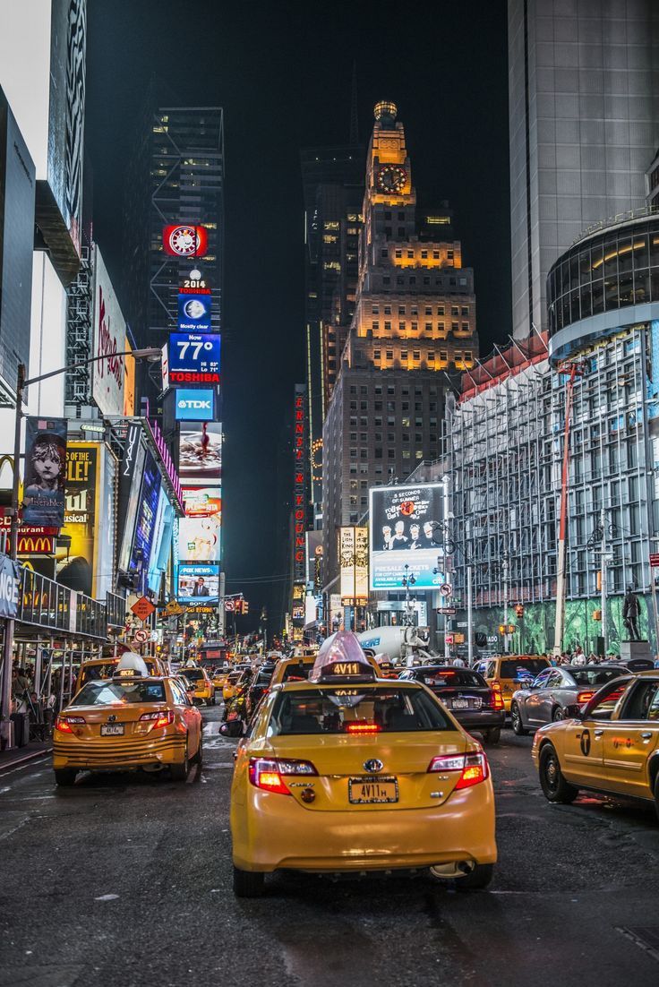 taxi cabs and taxis driving down a busy city street in new york at night