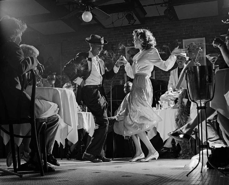 a woman in a dress dancing on stage with other people around her and one man holding a microphone