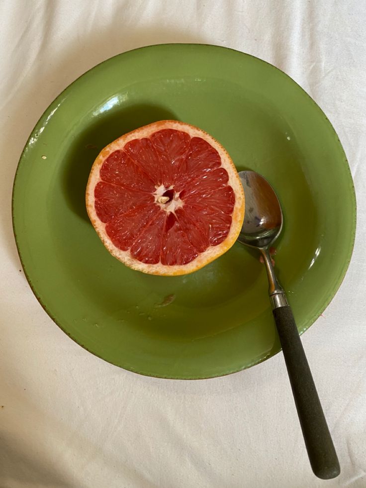 a grapefruit cut in half on a green plate with a spoon and knife