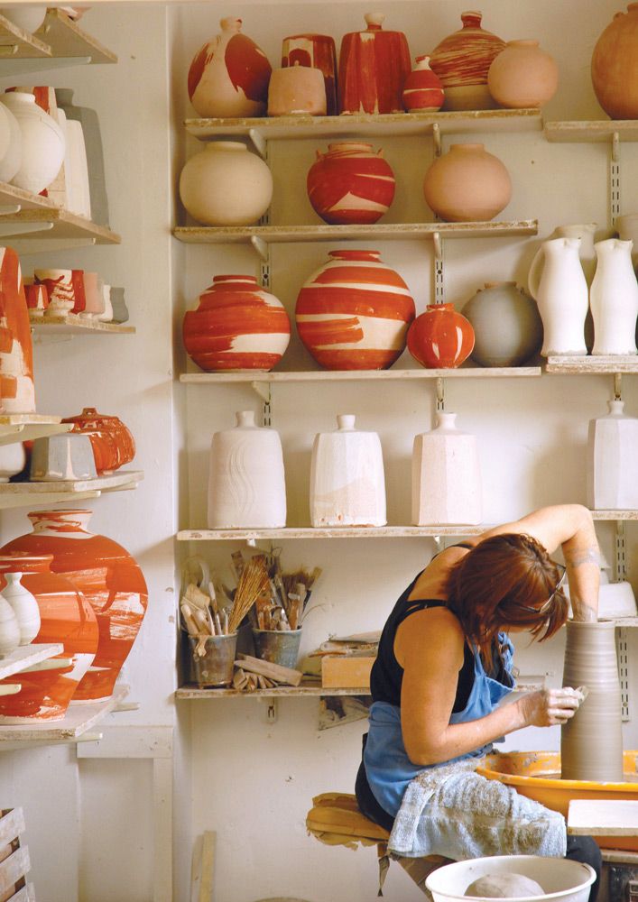 a woman sitting on a chair in front of shelves filled with vases and pottery