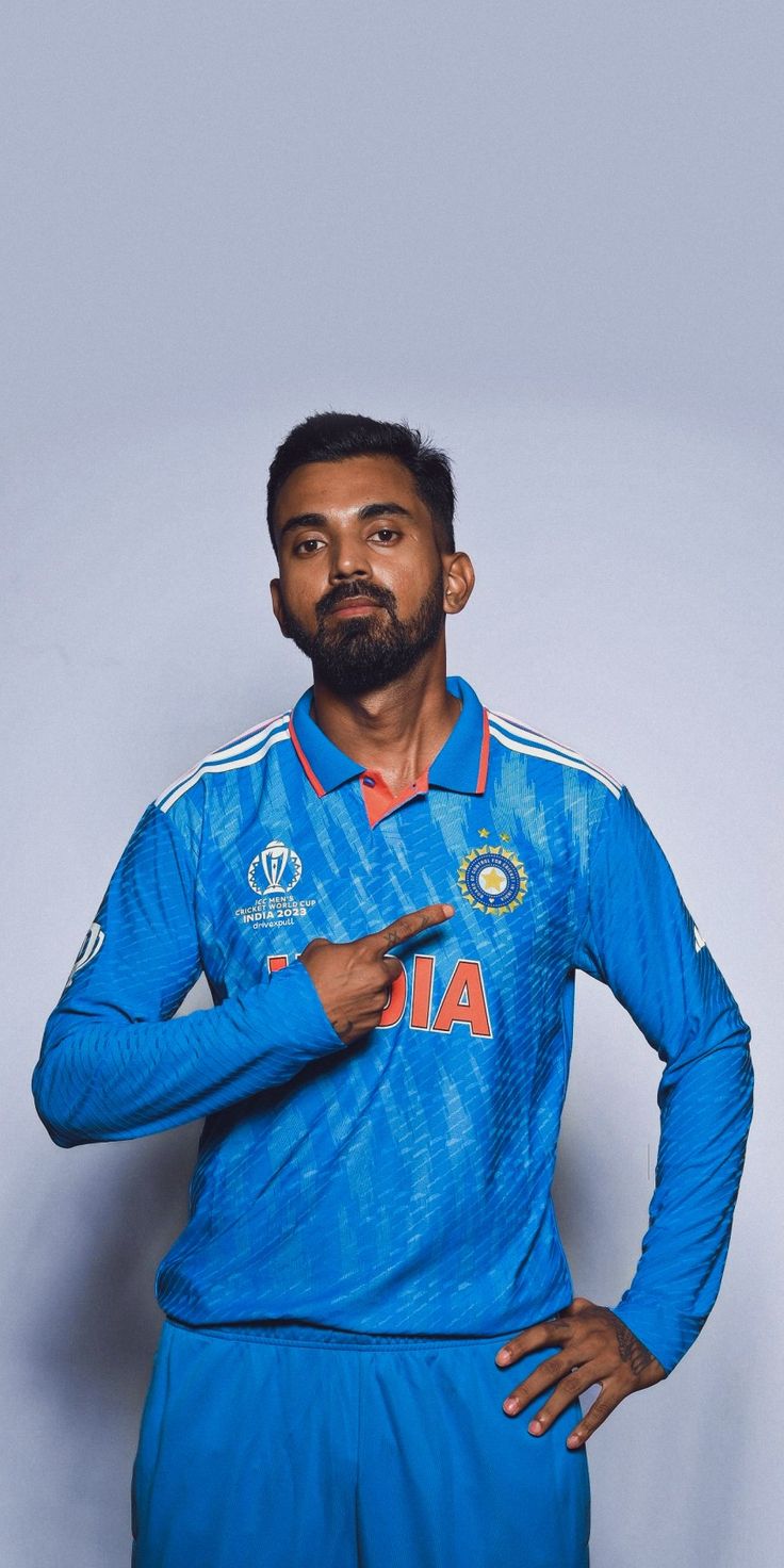 a man with a beard standing in front of a white wall wearing a blue uniform