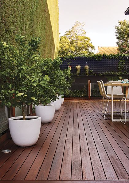 a wooden deck with potted plants and chairs on it, next to an outdoor dining area