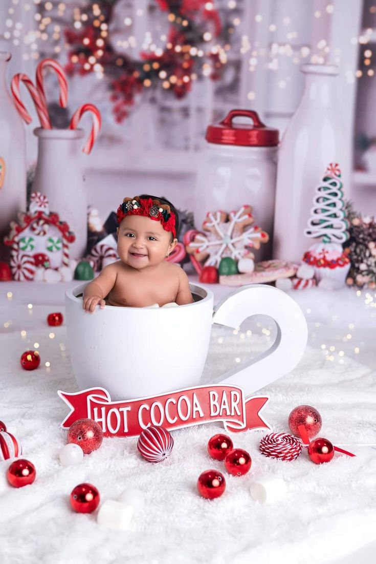 a baby sitting in a cup with candy canes around it and hot cocoa bar sign