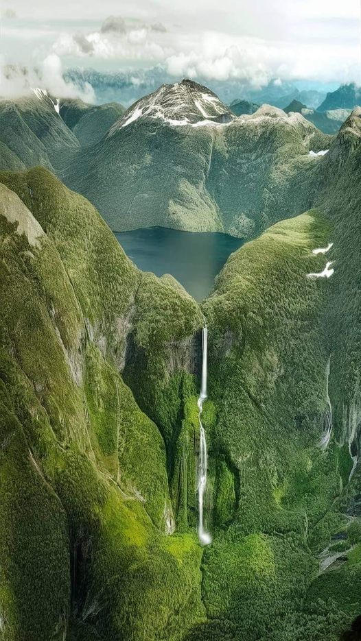 an aerial view of a waterfall in the middle of green mountains with water running down it