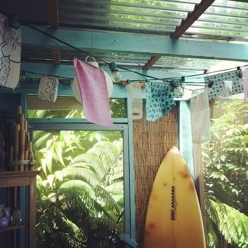 a yellow surfboard sitting in the corner of a room with plants and trees around it