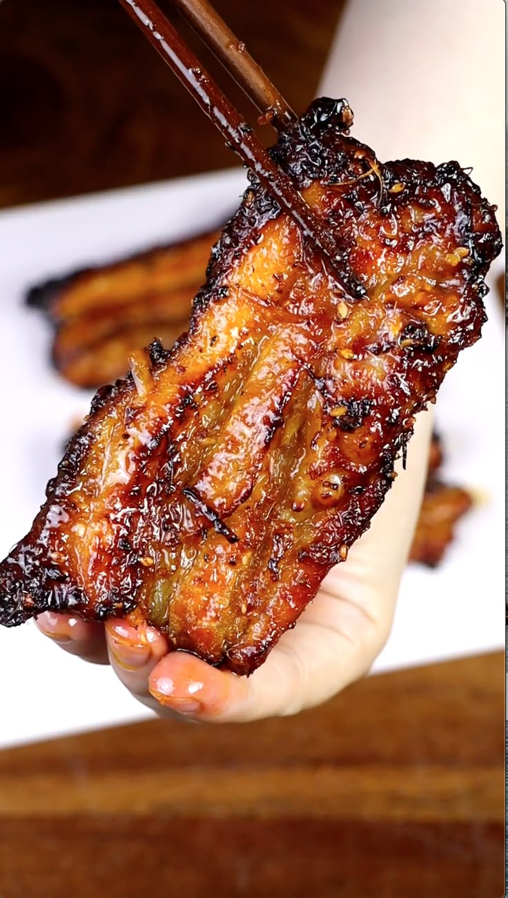 a person holding up a piece of meat with chopsticks in their left hand