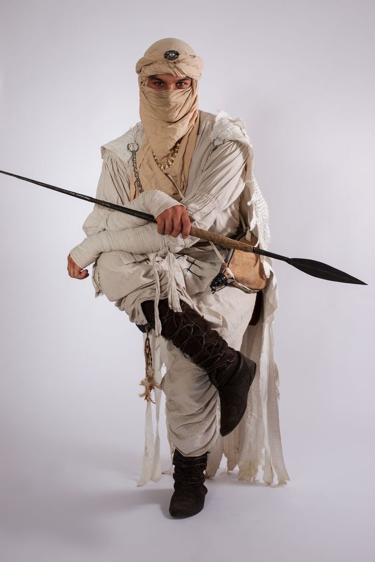 a man dressed as a warrior with two swords in one hand and a mask on the other