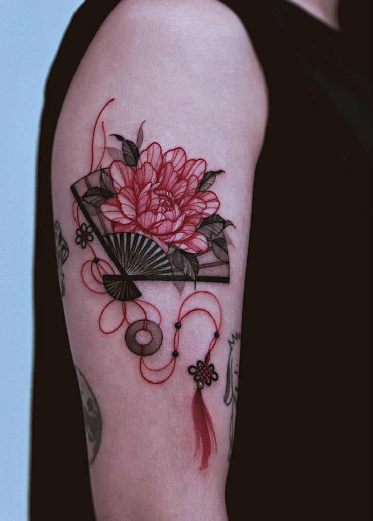 a woman with a tattoo on her arm holding a fan and pink flower in it