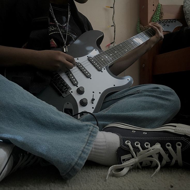 a person sitting on the floor with a guitar in their lap and his feet propped up