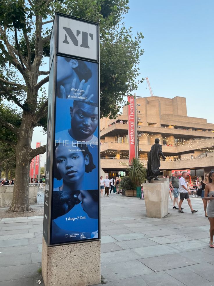 a large sign on the sidewalk in front of a building with people walking around it