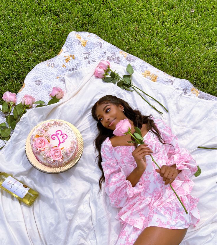 a woman laying in the grass with a cake and flowers next to her on a blanket