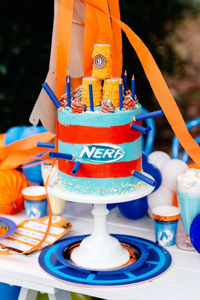 a nerf cake on a table with orange ribbon and blue plates, glasses and napkins