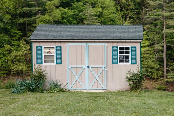 a small shed sitting in the middle of a lush green field with trees behind it