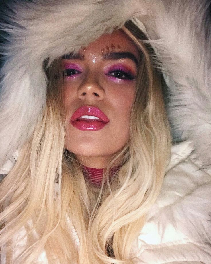 a woman with long blonde hair wearing a white fur coat and purple eyeshadow