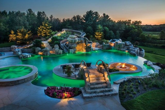 an aerial view of a pool at night with lights on the water and trees in the background