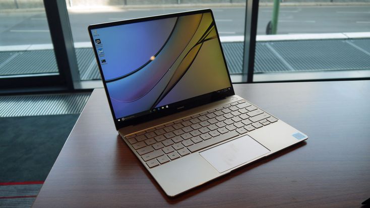 an open laptop computer sitting on top of a wooden table next to a large window