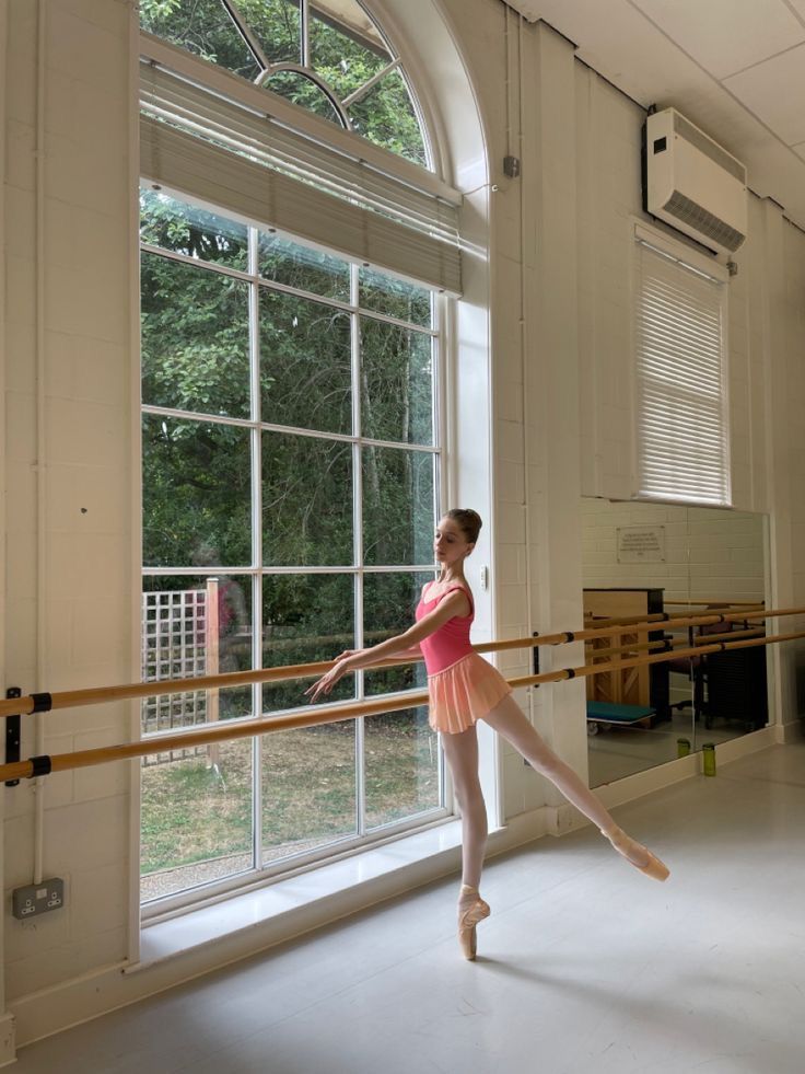 a young ballerina standing in front of a window