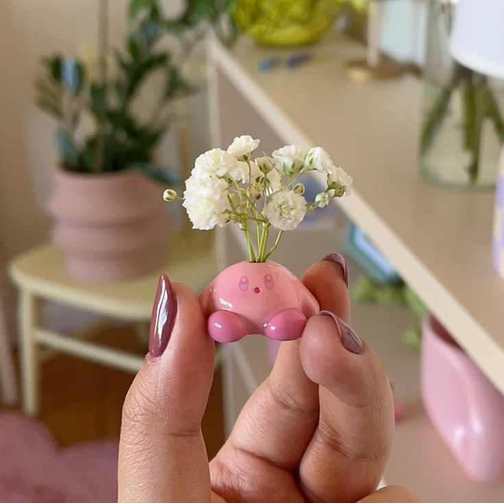 a person holding a tiny pink object with flowers in it