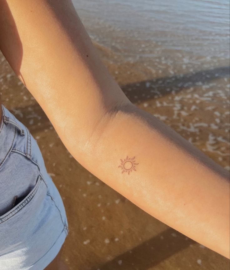 a woman's arm with a small sun tattoo on the left side of her arm