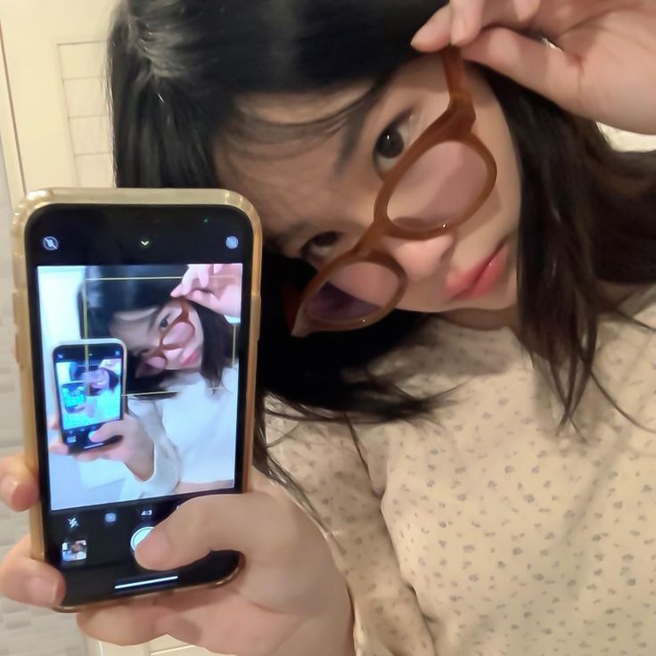 a woman holding up a smart phone to take a selfie with her eye glasses