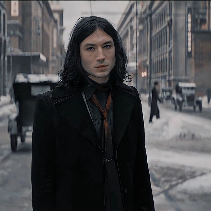 a man with long hair wearing a black coat and tie standing in the middle of a snowy street