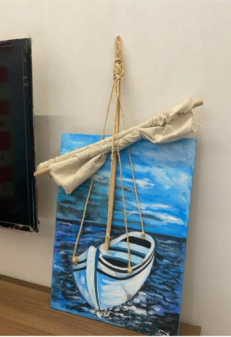 a painting hanging on the wall next to a framed canvas with a sailboat painted on it