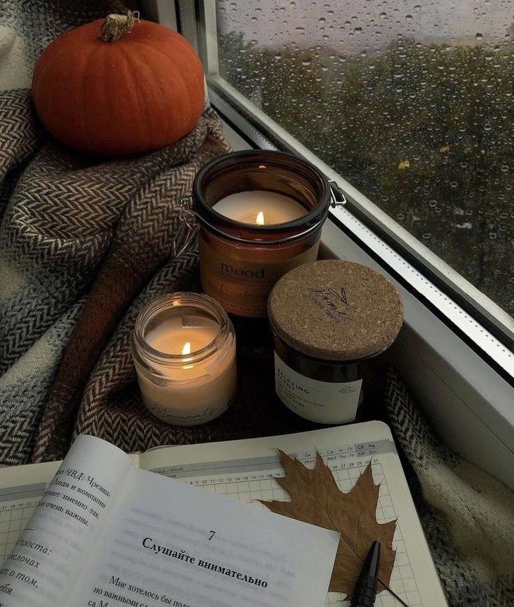 an open book sitting on top of a window sill next to candles and a pumpkin