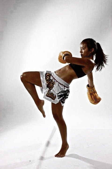 a woman in shorts and boxing gloves is posing for a photo while holding a punching mitt