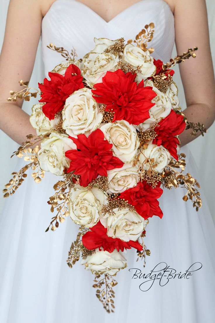 a bride holding a bouquet of red and white flowers with gold accents on her wedding day