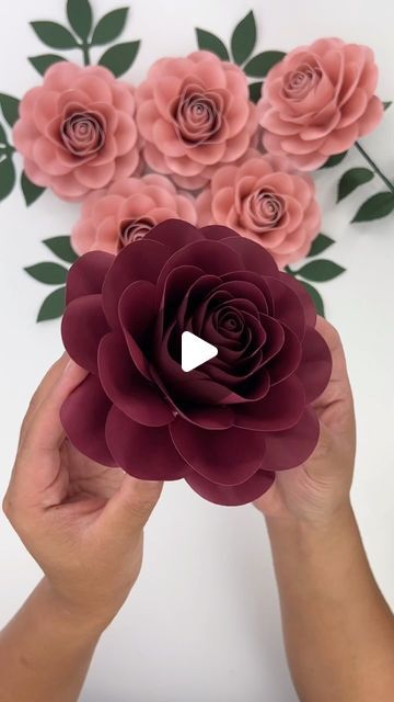 two hands holding paper flowers in front of a white background