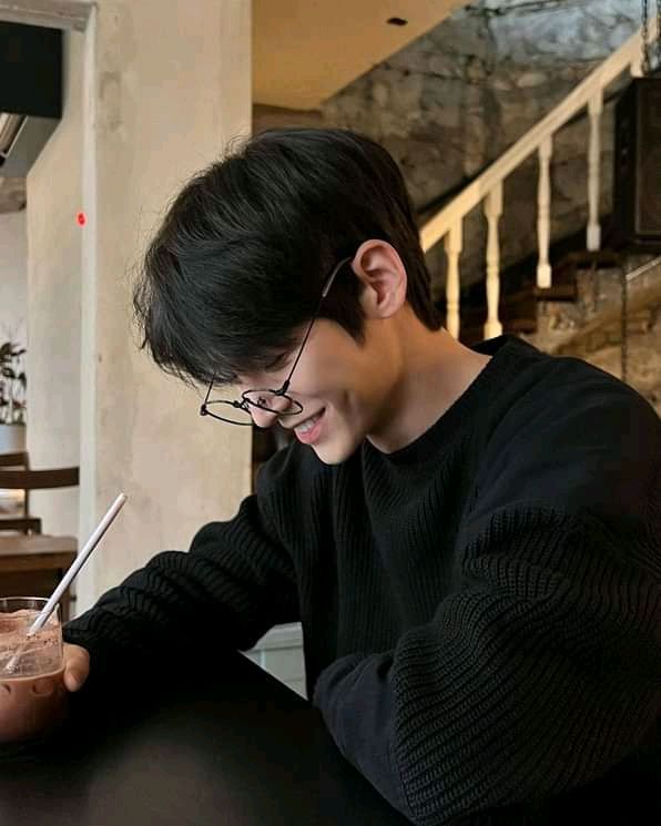 a young man sitting at a table with a drink and cell phone in his hand