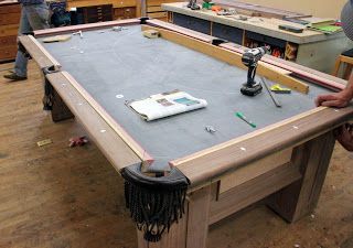 two men working on a pool table in a room full of woodworking supplies and tools