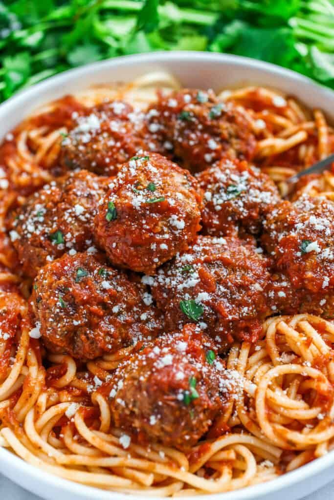 spaghetti and meatballs in a white bowl with parmesan sprinkled on top